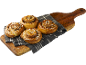 Fyra kanelbullar, strödda med pärlsocker, på en duk på en skärbräda.