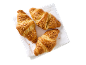 Tre gyllenbruna croissanter toppade med hackade nötter, på en vit servett.
