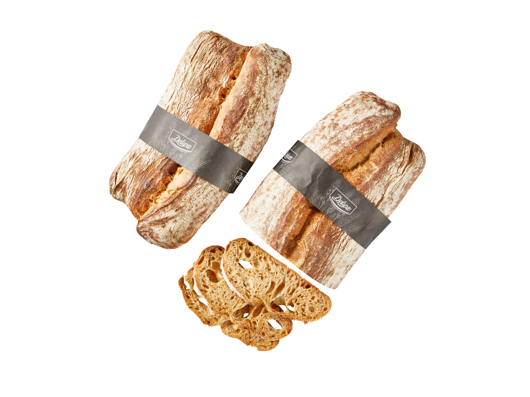 Två rustika bröd med 'Deluxe'-band, ett skivat, på svart bakgrund.