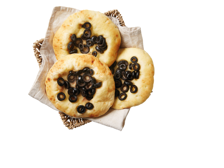 Focaccia med svarta oliver i en flätad korg med en linneduk.