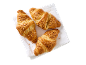 Tre gyllenbruna croissanter toppade med hackade nötter, på en vit servett.
