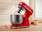 Röd köksmaskin med skål i rostfritt stål, ägg och bakingredienser.