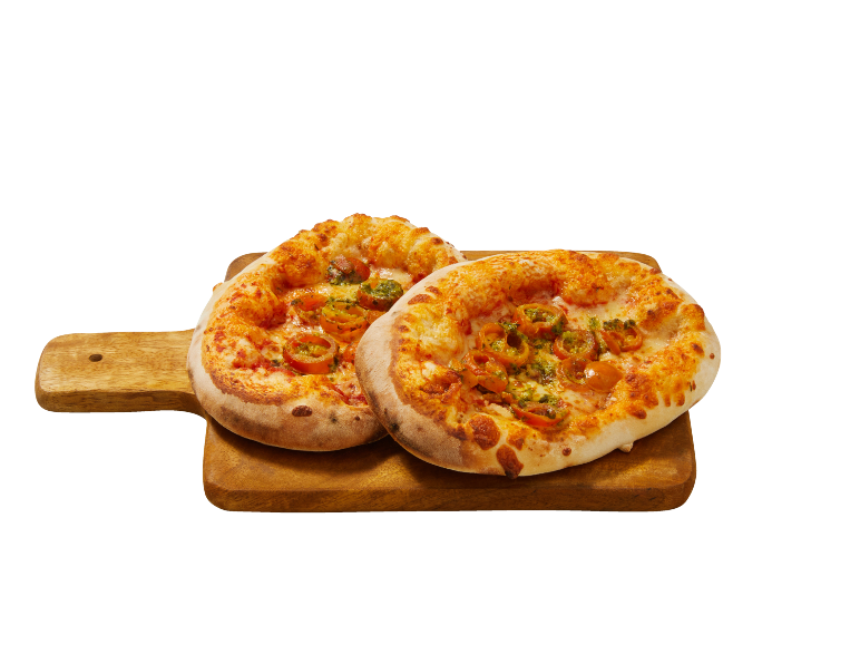 Två nybakade minipizzor med tomater och pesto på en skärbräda i trä.