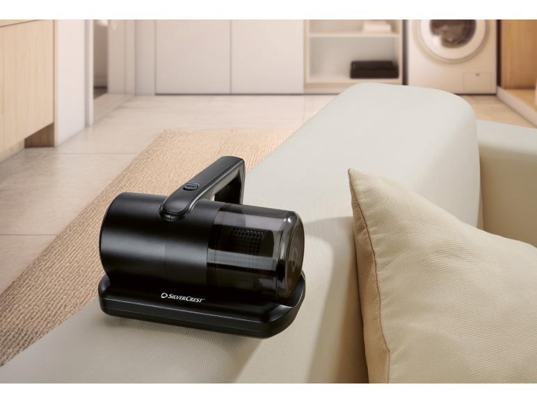 Svart handdammsugare på en ljus soffa med en kudde, i en modern interiör.