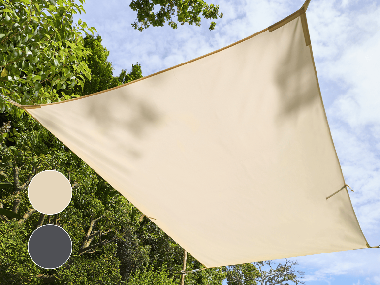 Beige solsegel spänt över en grön trädgård under en blå himmel.