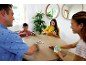Familj spelar ett kortspel vid ett träbord, leende och engagerade.