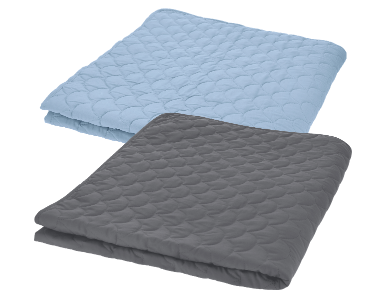 Två quiltade madrasskydd, ett ljusblått och ett mörkgrått, vikta på svart bakgrund.
