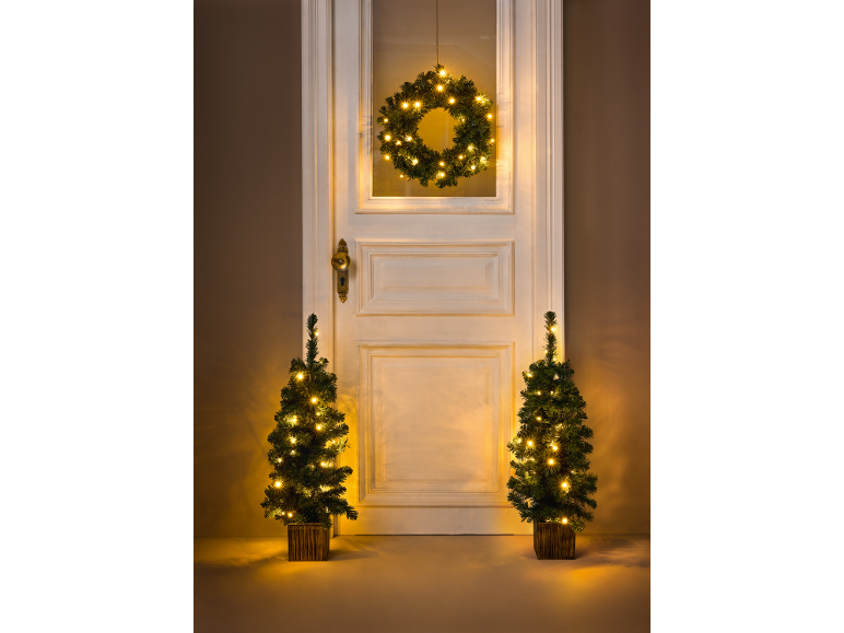 Belyst julkrans på dörren och två små julgranar med ljus.