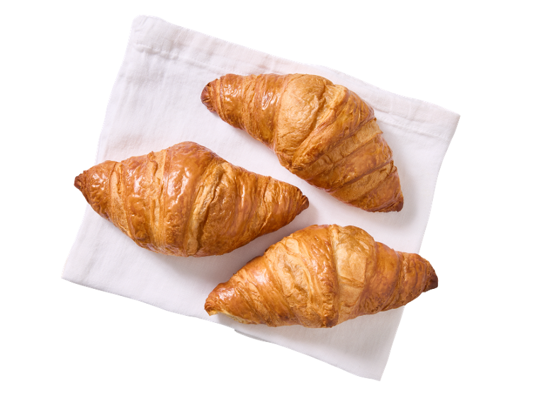 Tre gyllenbruna croissanter på en vit servett, sedda ovanifrån.