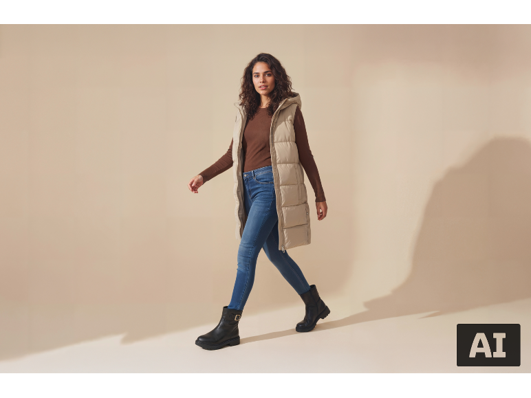 Kvinna i lång beige väst, brun tröja, jeans och svarta stövlar