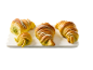 Fyra gyllene croissanter med pistagefyllning och vit glasyr på en bräda.