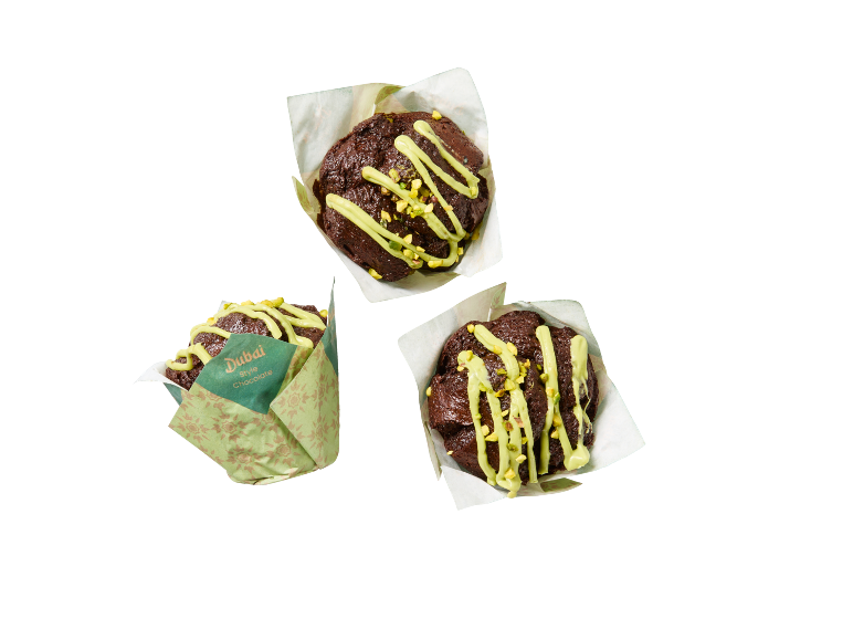 Tre chokladmuffins med grön glasyr och pistageströssel, en i 'Dubai Style Chocolate' förpackning.