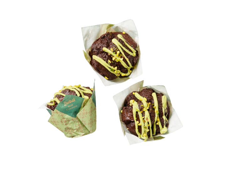 Tre chokladmuffins med grön glasyr och pistageströssel, en i 'Dubai Style Chocolate' förpackning.