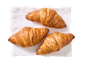 Tre gyllene croissanter på en vit linneservett.