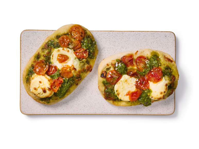 Två mini pizzor med pesto och tomat på en rektangulär tallrik.