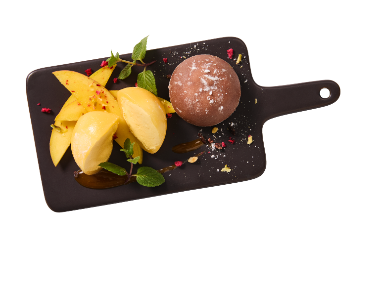 Dessert med färsk mango, mangoglass och en chokladboll på en bräda.