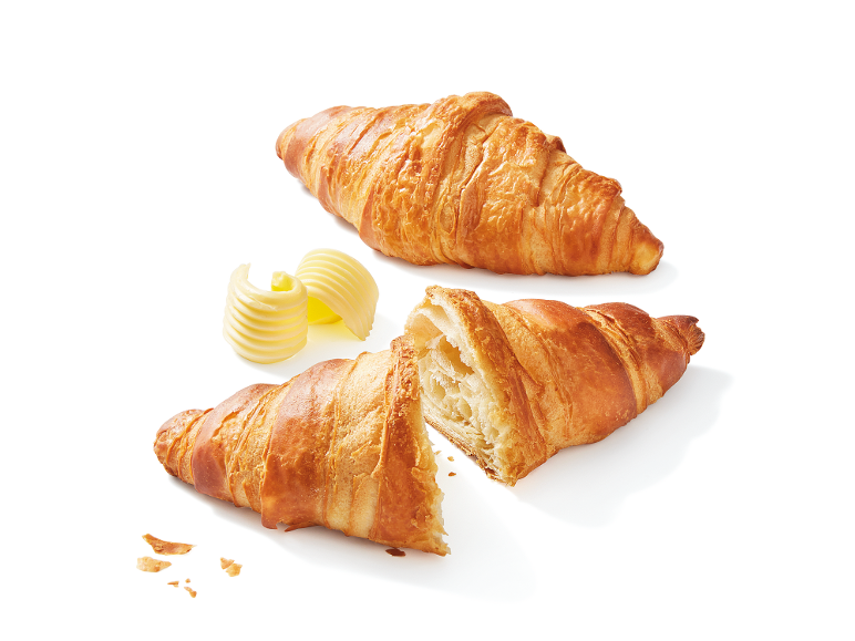Gyllene croissanter med smör, en hel och en halverad.