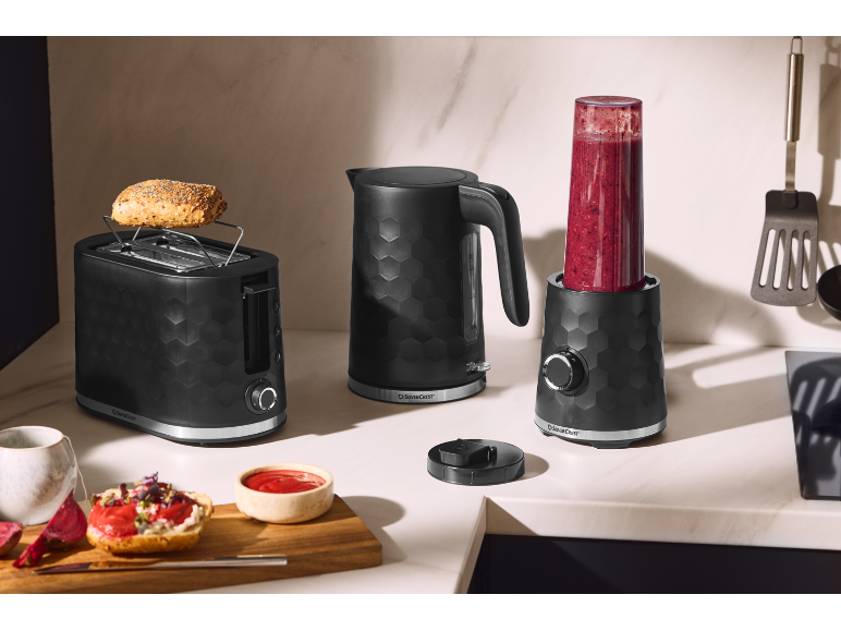 Svart brödrost, vattenkokare och mixer med smoothie på köksbänken.