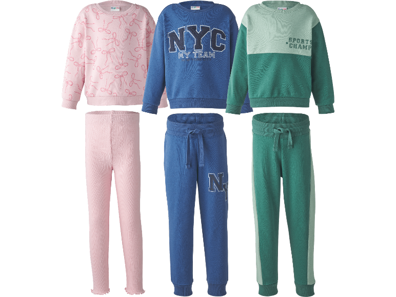 Tre uppsättningar barnmjukisar: rosa med rosetter, blå med 'NYC MY TEAM' och grön med 'SPORTS CHAMP'.