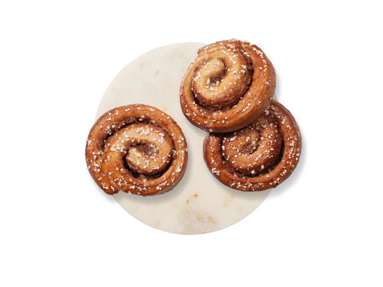 Tre kanelbullar med pärlsocker på en rund marmorbricka.