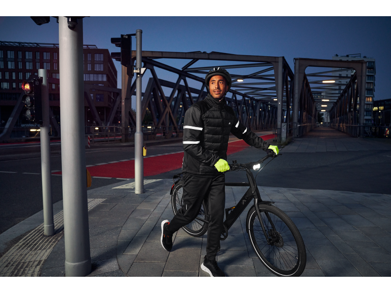 Man cyklar i staden på natten, bär en reflekterande cykeljacka och handskar.