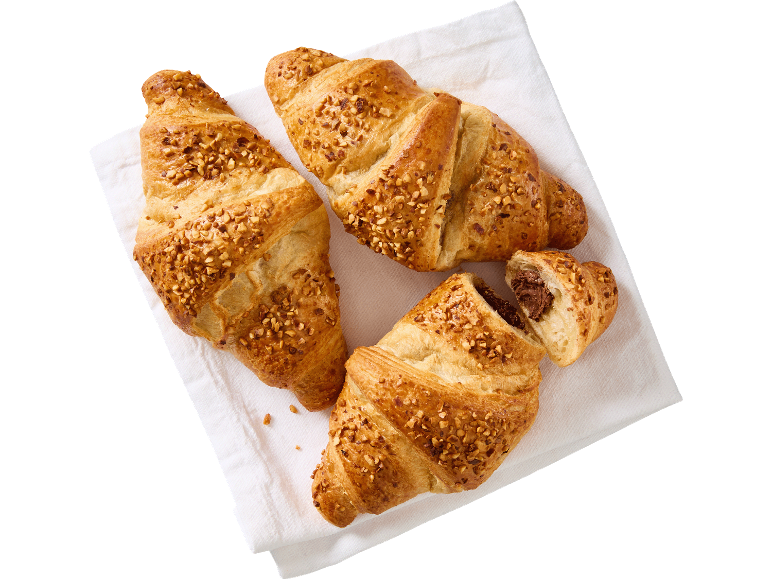 Tre croissanter med nötter, en fylld med choklad, på en vit duk.
