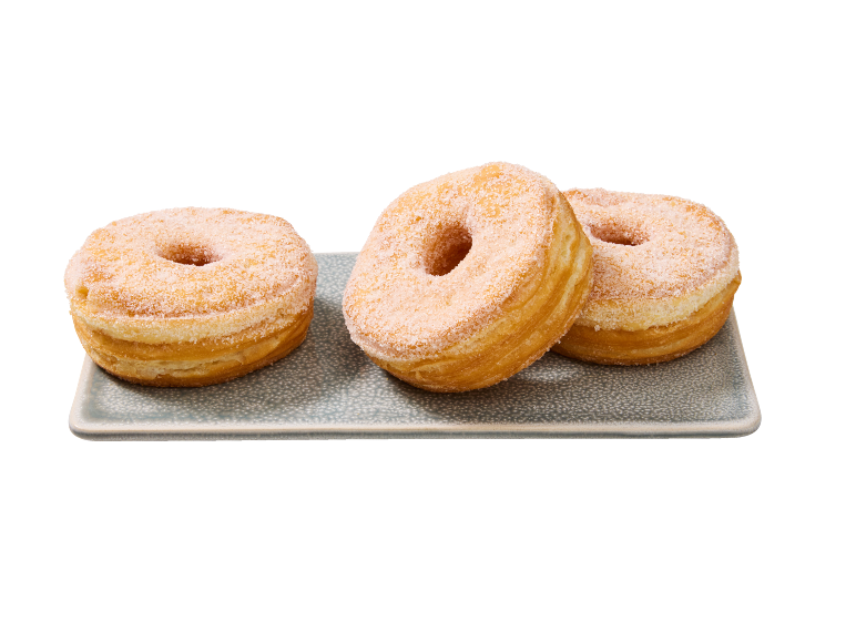 Tre sockerströdda cronuts på ett grått serveringsfat mot svart bakgrund