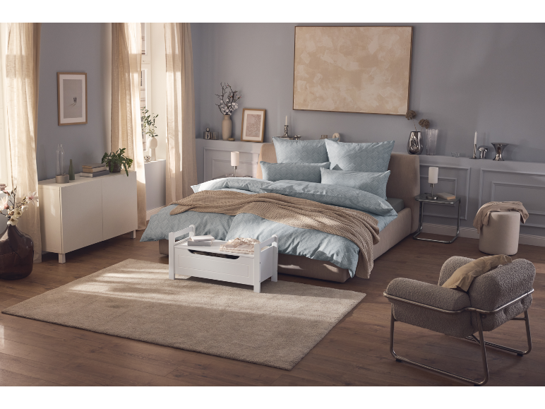 Modernt sovrum med dubbelsäng, blå sängkläder, beige matta och en bekväm fåtölj.