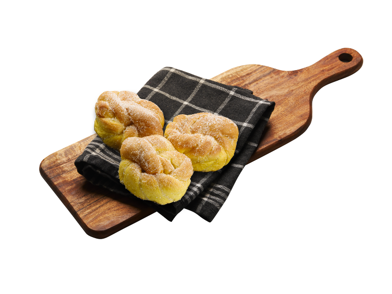 Tre gyllene söta bullar, strödda med socker, på en svart servett och träskärbräda.
