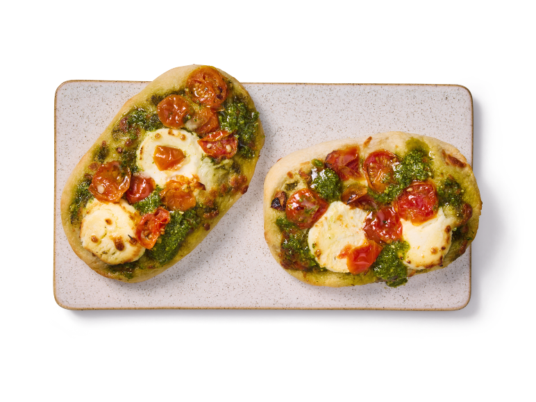 Två minipizzor med pesto, körsbärstomater och mozzarella på en rektangulär tallrik.