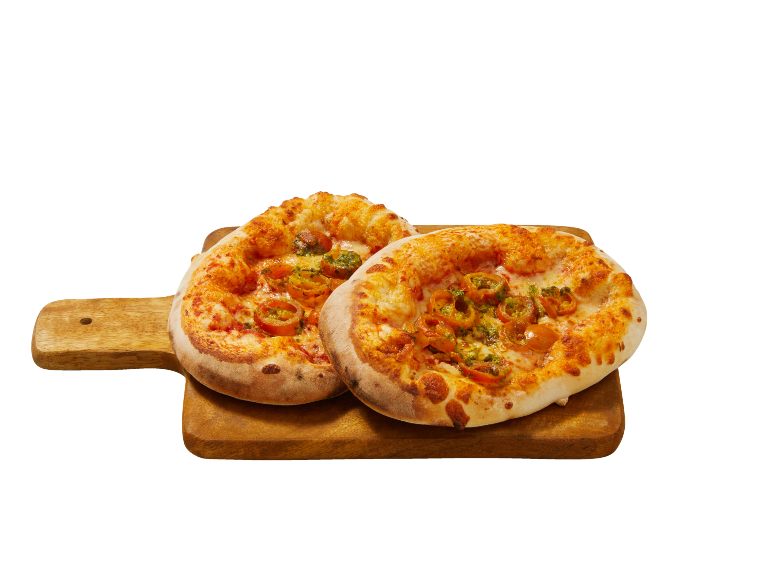 Två nybakade minipizzor med tomater och pesto på en skärbräda i trä.