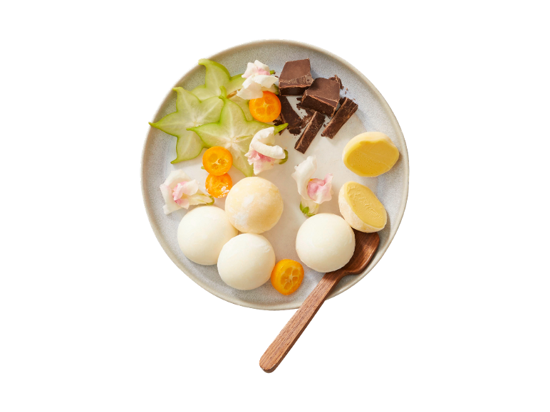 Dessert med glasskulor, stjärnfrukt, kumquats, blommor och choklad på en tallrik.