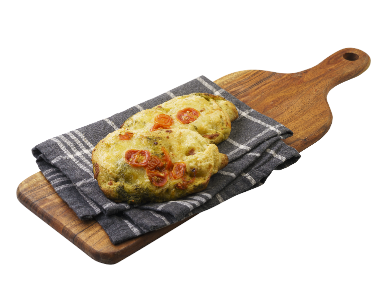 Focaccia med pesto och körsbärstomater på en träskärbräda och kökshandduk.