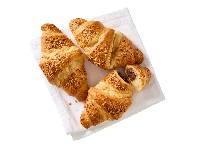 Tre croissanter med nötter på en vit handduk, en med chokladfyllning.