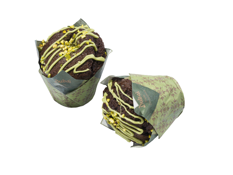 Två chokladmuffins med grön glasyr och hackade pistagenötter, inslagna i grönt papper.