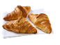 Tre gyllene, krispiga croissanter på en vit duk.