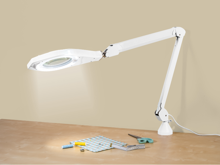 Vit LED-förstoringslampa över ett bord med symaterial.