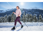 Kvinna i rosa jacka och lila leggings vandrar i snöigt bergslandskap.
