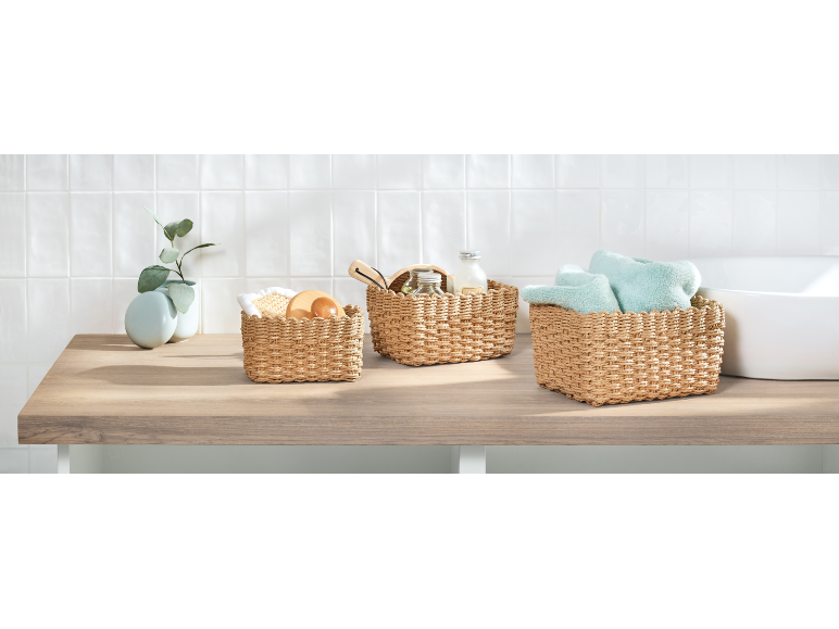 Flätade korgar med badprodukter och en växt på en träbänk.