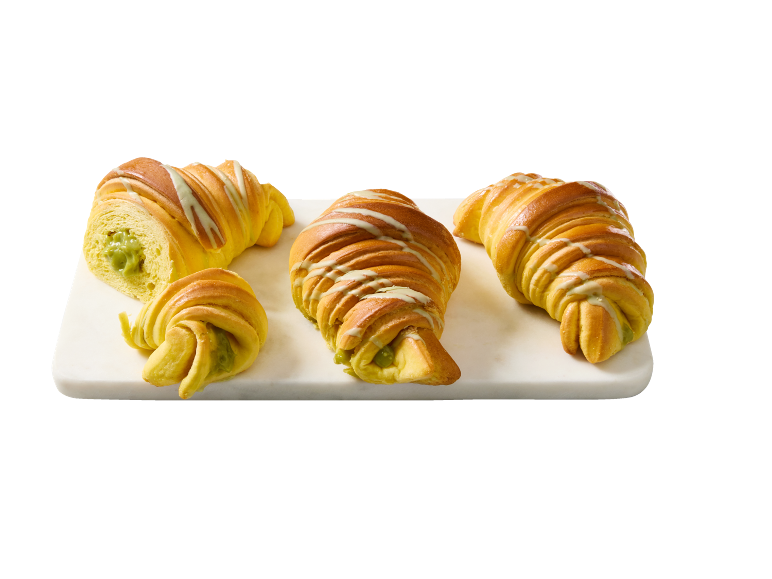 Fyra gyllene croissanter med pistagefyllning och vit glasyr på en bräda.