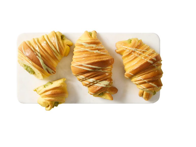 Fyra gyllene croissanter fyllda med pistage och dekorerade med ljusgrön glasyr på en vit bräda.