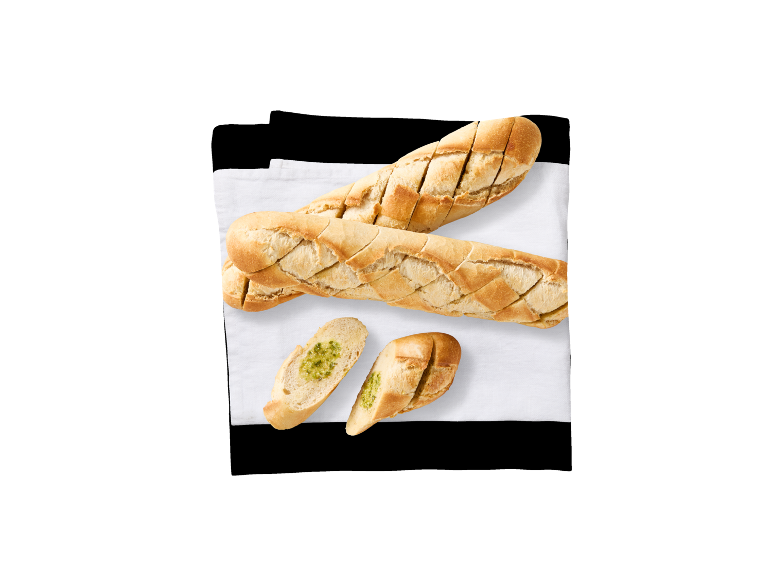 Två skivade baguetter och två baguetteskivor med pesto på en vit duk.