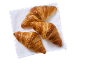 Tre gyllenbruna croissanter på en vit servett, sedda ovanifrån.