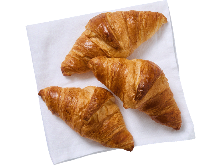 Tre gyllene, krispiga croissanter på en vit servett.