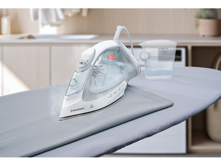 Ångstrykjärn på strykbräda med vattenmått.