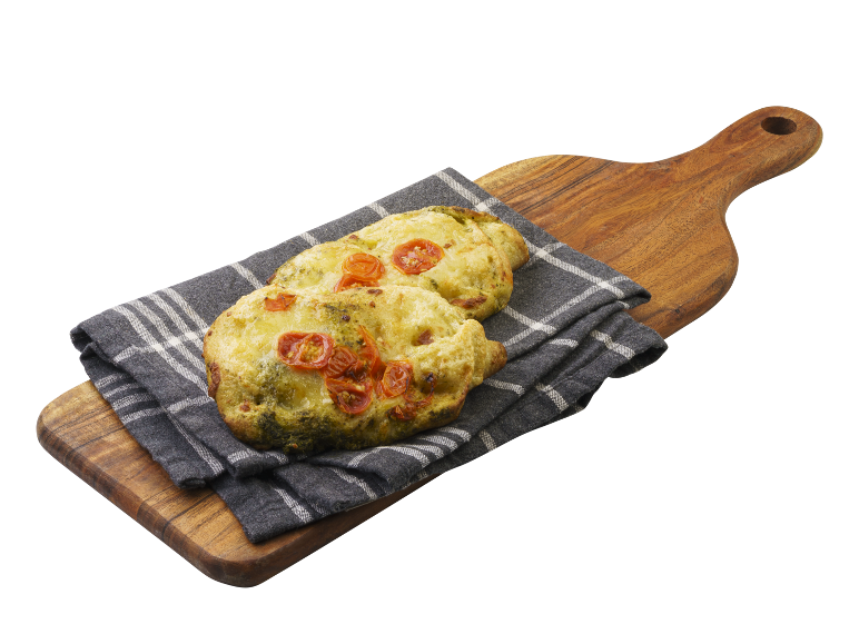 Focaccia med pesto och körsbärstomater på en träskärbräda och kökshandduk.