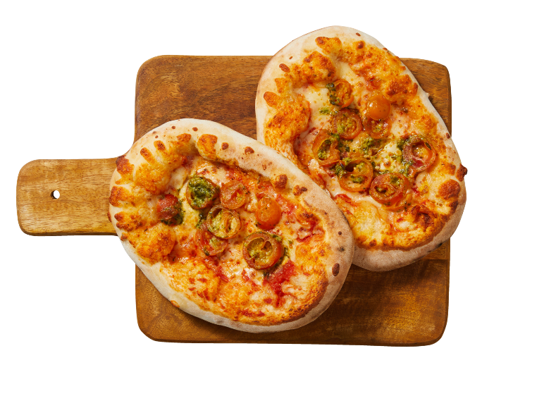 Två minipizzor med tomater och pesto på en träskärbräda.