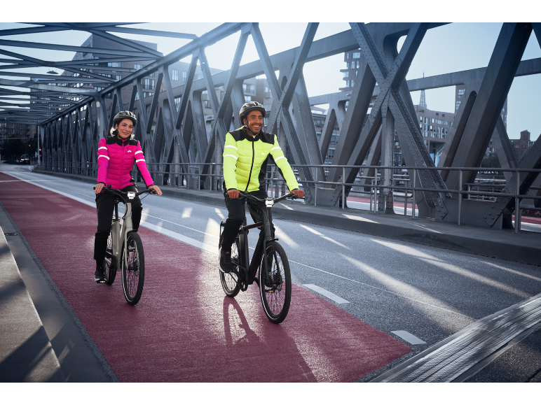 Par på elcyklar i reflexjackor på en bro.