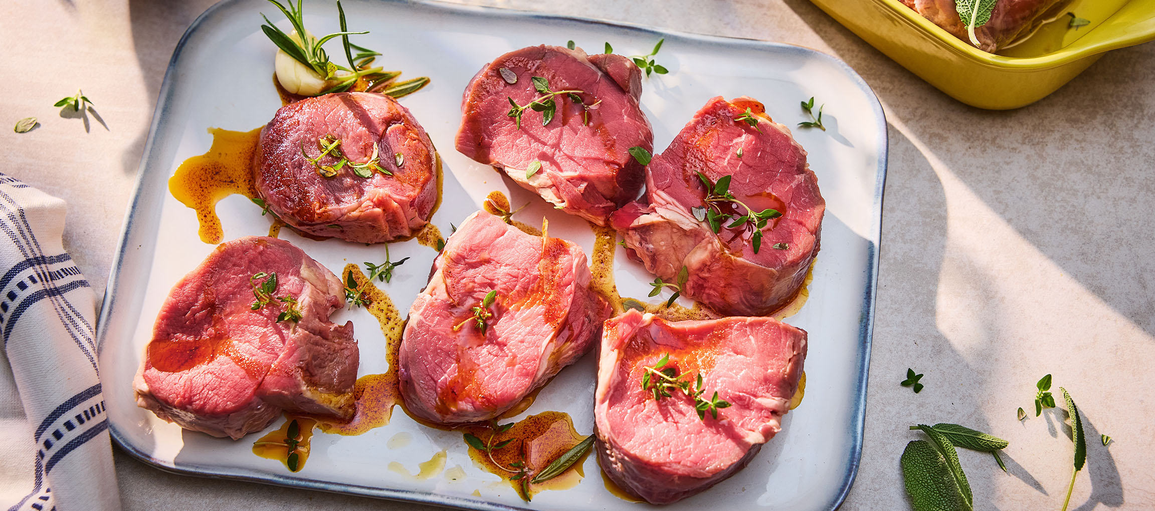 Färska biffstekar med örter och olja på ett vitt fat.
