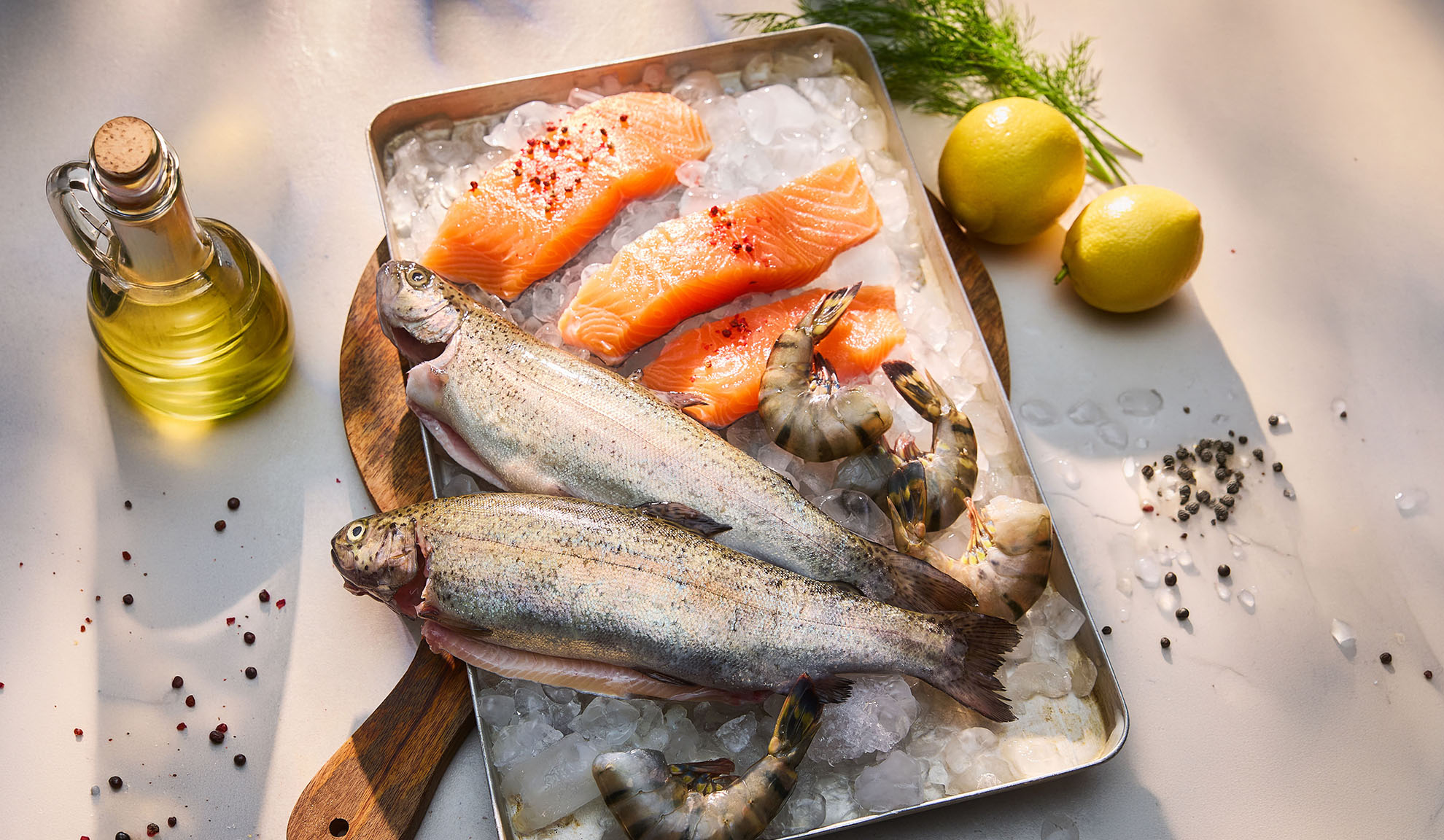 Färsk fisk, laxfiléer och räkor på is, med citroner och olja.